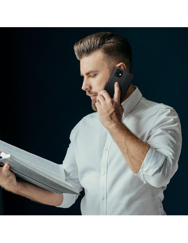 Man som pratar i telefon med Motorola Moto E20 i plånboksfodral, hållande en bok