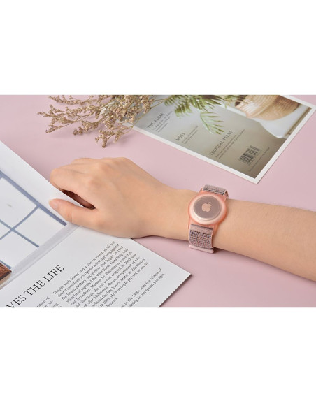 Nylonarmband för Airtag i rosa, bärs på handleden med en tidning i bakgrunden