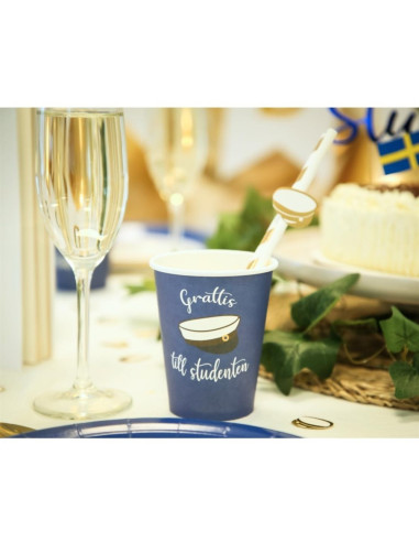 Blå pappersmugg med studentmotiv och text, placerad på festbord med glas och dekorationer