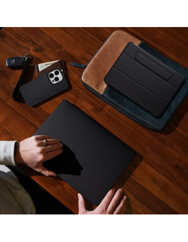 Mörkgrönt iPhone 15 Pro skal i veganläder, liggande på ett bord med en hand som rör vid en laptop