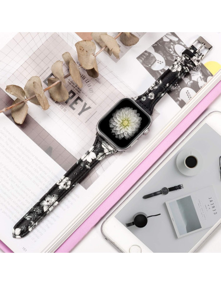 Svart läderarmband med vit blomma, visat på en Apple Watch med blommotiv, omgiven av tidningar och en telefon